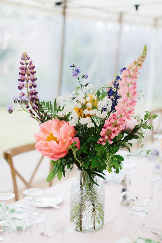 a bright wedding centerpiece of blush, purple, white blooms, a large pink peony and greenery is a gorgeous idea for a summer wedding
