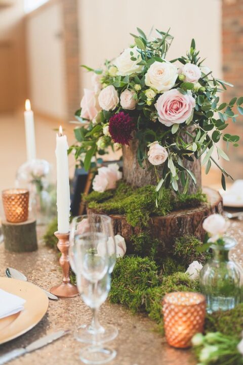 a chic enchanted forest wedding centerpiece of moss, tree stumps, blush roses and burgundy dahlias, tall and thin candles