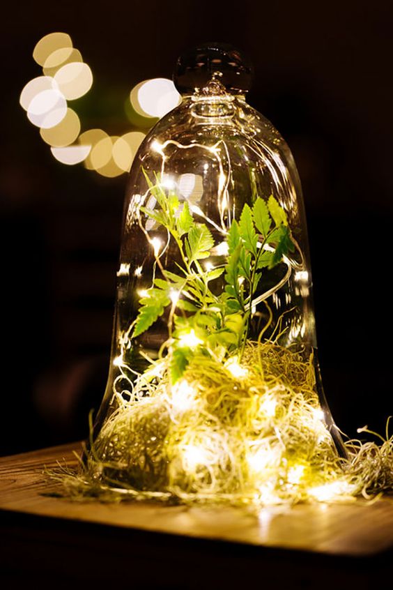 a cloche with some hay, greenery and lights is a lovely idea for an enchanted forest wedding