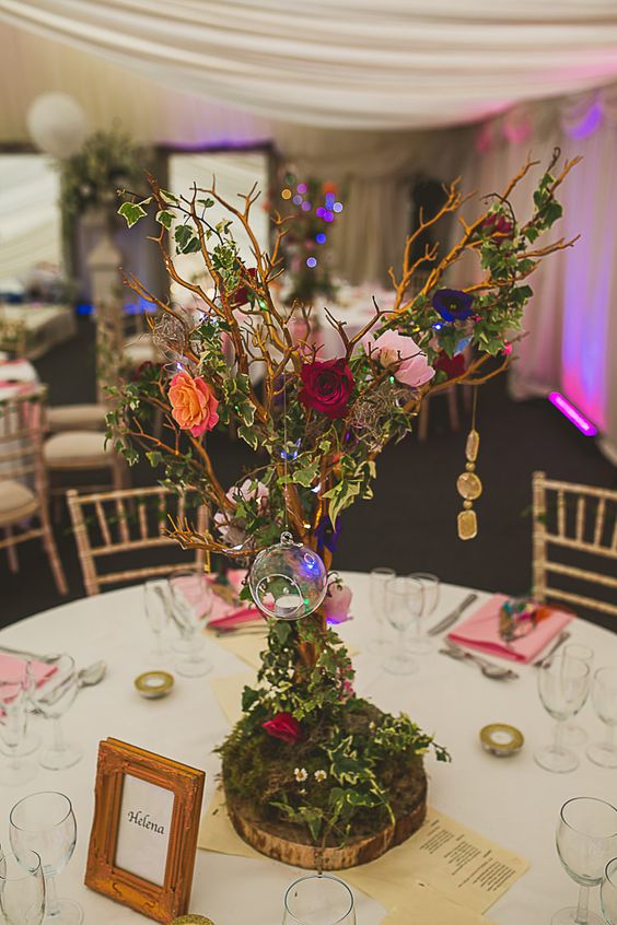 a colorful and lovely enchanted forest wedding centerpiece of a tree with bold blooms, candles, leaves and rhinestones hanging on one branch