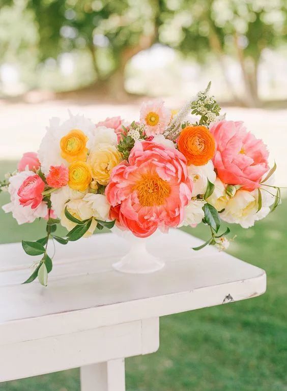 a colorful summer wedding centerpiece of yellow and pink ranunculus, white blooms and pink peonies and greenery