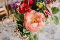 a colorful wedding centerpiece of a pink peony, red poppies, yellow and blue blooms and purple ones, greenery is a lovely idea for summer