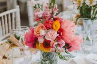 a colorful wedding centerpiece of large pink peonies, yellow roses, pink flowers and sunflowers and greenery is a lovely idea for a colorful summer wedding