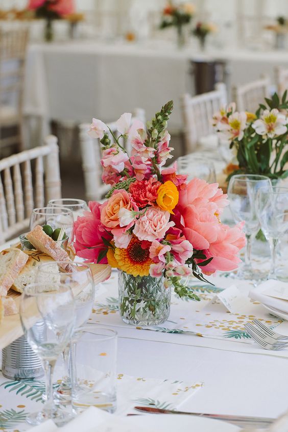 a colorful wedding centerpiece of large pink peonies, yellow roses, pink flowers and sunflowers and greenery is a lovely idea for a colorful summer wedding