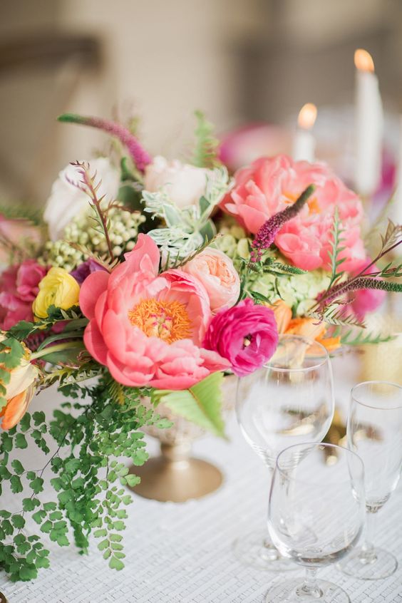 a colorful wedding centerpiece of pink peonies, blush peony roses, fuchsia ranunculus, lots of greenery and berries for summer