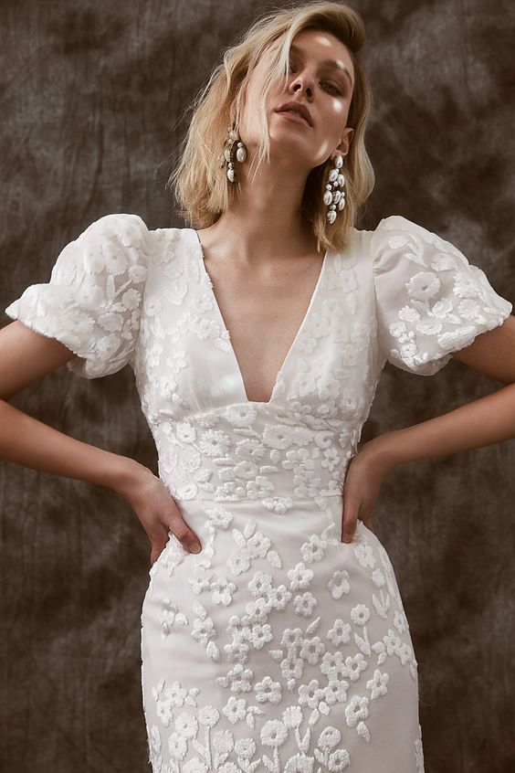 a delicate and sophisticated bridal look with a lace applique fitting wedding dress with a V-neckline and puff sleeves plus statement earrings