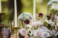 a fab enchanted forest wedding centerpiece of a moss runner, books, tall and thin candles, lilac and blush blooms and cloches with them