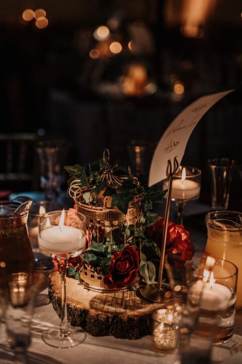 a fantastic enchanted forest wedding centerpiece with a wood slice, a cage with greenery and burgundy roses, candles and a table name