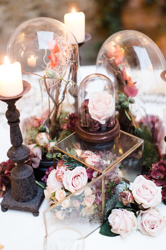 a gorgeous enchanted forest wedding centerpiece of a glass box with pink and purple blooms, cloches with branches and candles around