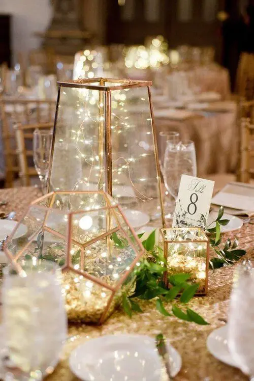 a gorgeous enchanted forest wedding centerpiece of candle lanterns with lights, greenery and a table number is amazing