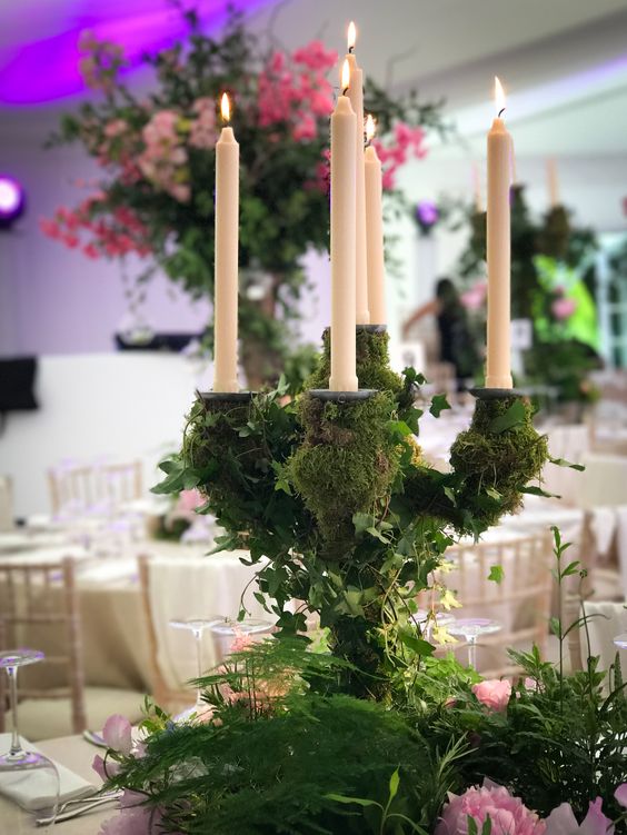 a large candelabra covered with foliage and moss, with pillar candles and pink blooms around as an enchanted forest wedding centerpiece