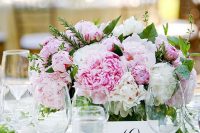 a lovely summer wedding centerpiece of white and pink peonies and greenery, small candles around is a cool piece and you can DIY it