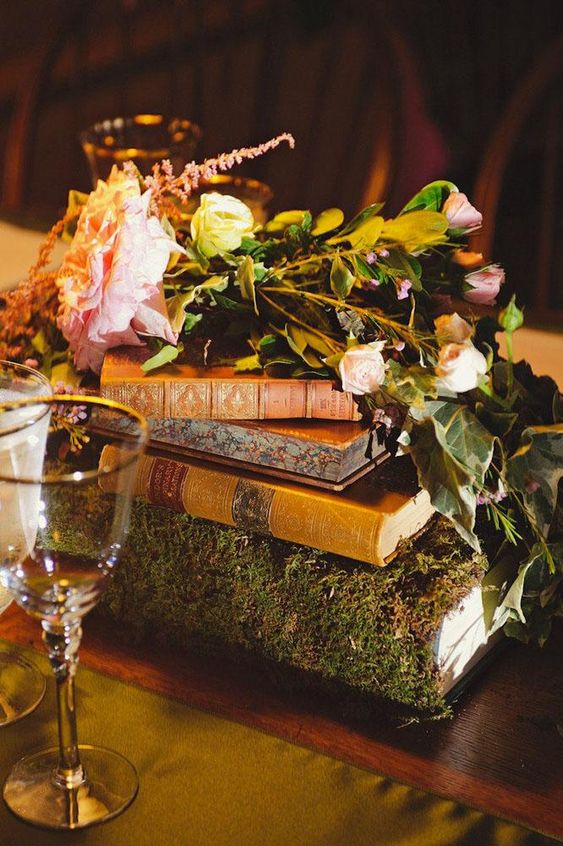 a lovely wedding centerpiece of vintage books including a moss covered one, with greenery, pink and white flowers