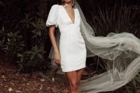 a modern plain mini wedding dress with a deep neckline, puff sleeves, white mules, pearl earrings and a long veil for a retro-inspired look