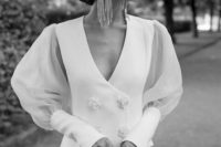 a sophisticated and modern bridal look with a white blazer dress with semi sheer puff sleeves and embellished buttons, statement earrings and a hat