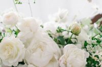 a sophisticated wedding centerpiece of white peonies and ranunculus plus greenery is a gorgeous idea for an all-white wedding