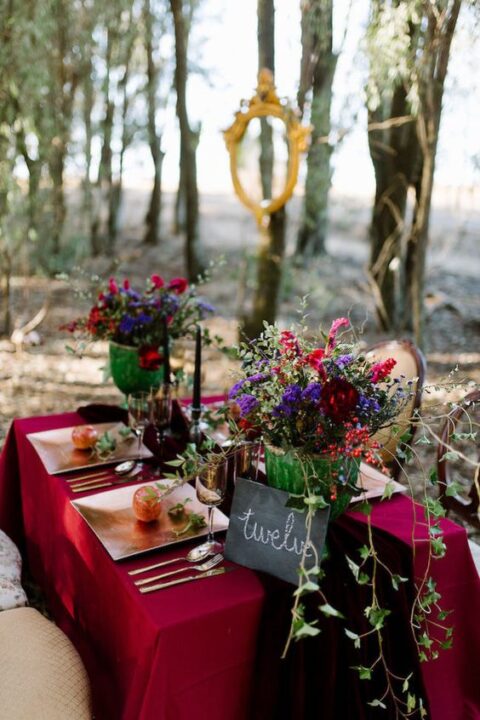 a super bold jewel tone wedidng centerpiece of burgundy, red and purple blooms and cascading greenery is amazing for a fall enchanted forest wedding