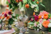 a super lush and bold wedding centerpiece of pink peonies, light pink roses, orange tulips and lots of greenery in a tall silver vase