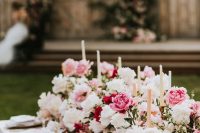 a super lush wedding table runner with white, light pink and bold pink peonies and roses and tall and thin candles is amazing for summer