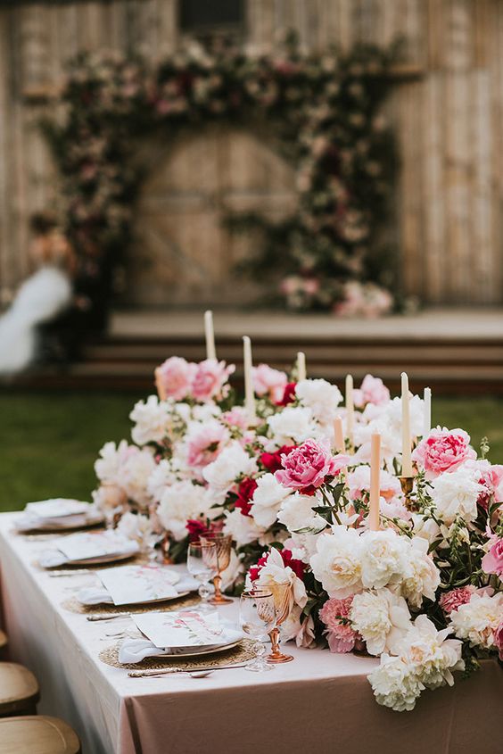 a super lush wedding table runner with white, light pink and bold pink peonies and roses and tall and thin candles is amazing for summer