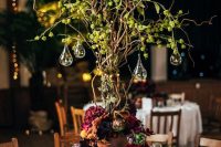 a whimsical enchanted forest wedding centerpiece of a vine tree with greenery, drops with candles, bold blooms at the base of the tree
