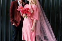 an 80s bridal look with a plain pink midi dress with puff sleeves, white trainers and socks, a pink veil and a pink wedding bouquet