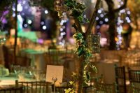 an enchanted forest wedding centerpiece of a tree with leaves and candle lanterns plus moss at the base of the tree