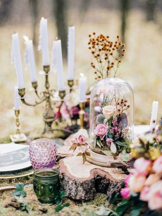 an enchanted forest wedding centerpiece of moss, a wood slice, a cloche with blooms and foliage and candles around