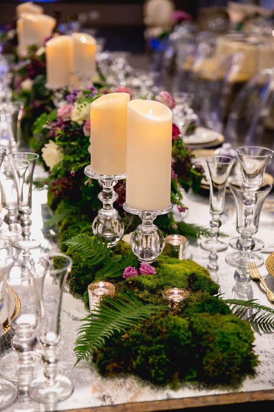 an enchanted forest wedding centerpiece of moss, bright pink blooms, fern, candles and pillar candles is a chic and bold idea