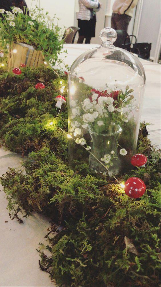 an enchanted forest wedding centerpiece of moss, lights, mushrooms, a cloche with white blooms is a lovely decoration to compose
