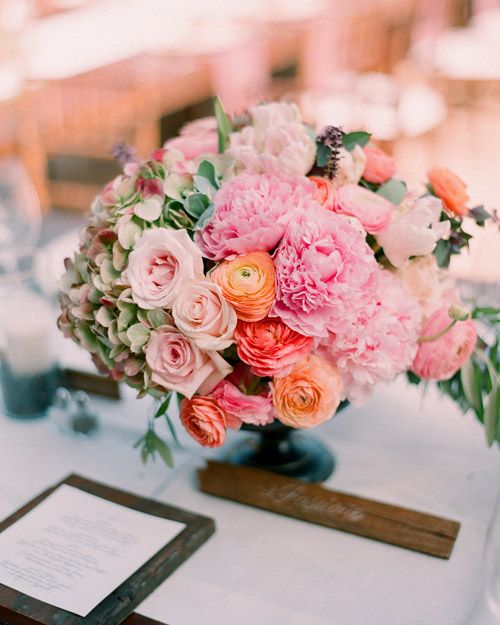 an eye catchy wedding centerpiece of green hydrangeas, pink peonies, orange ranunculus and blush roses, greenery is a very textural arrangement