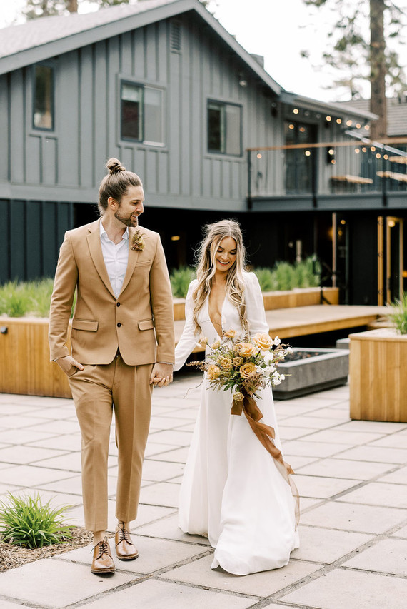 a minimalist bridal look with a plain wedding dress, a plunging neckline and puff sleeves, a groom wearing a beige suit, beige shoes and a white shirt