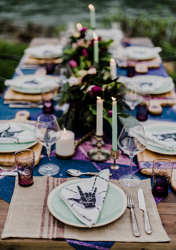 a bold boho rock n roll wedding tablescape done in purple and blue, with purple and blush blooms, neutral and mint green candles and plates