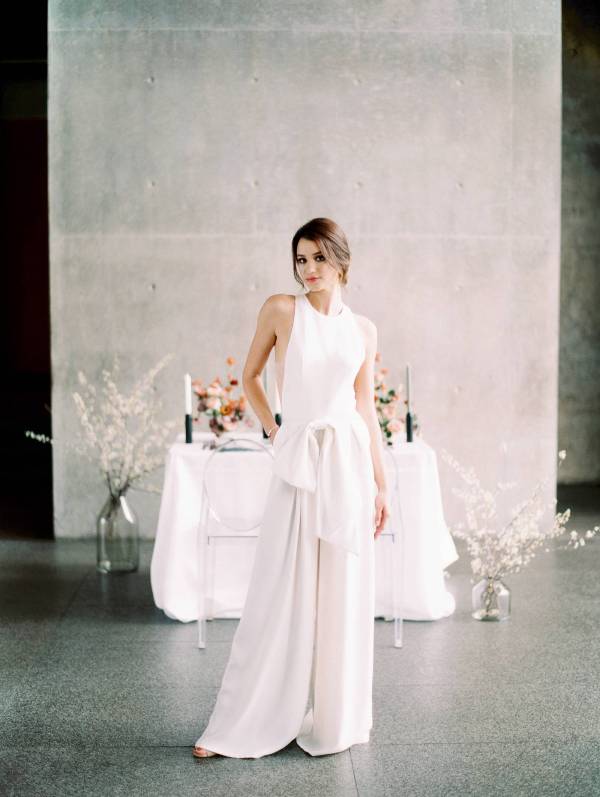 a chic minimalist bridal look with a sleeveless jumpsuit with a halter neckline, wideleg pants and a large bow on the waist