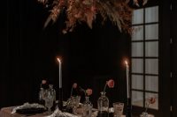 09 a chic moody rock wedding tablescape with a dusty pink tablecloth, black plates, black vases and candleholders, a grass and bloom overhead isntallation