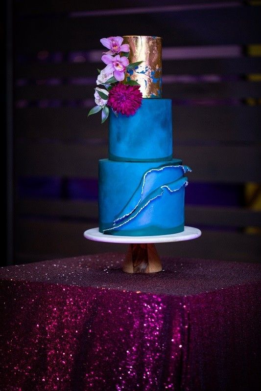 a bold wedding cake with bold blue tiers and a gold leaf one, with pink and fuchsia blooms and rough edges is wow