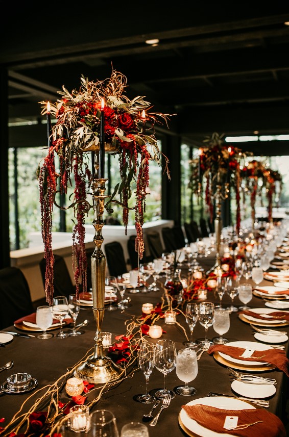 a Gothic meets rock tablescape with tall floral centerpiece and black candles, red petals and candles on the table, red napkins