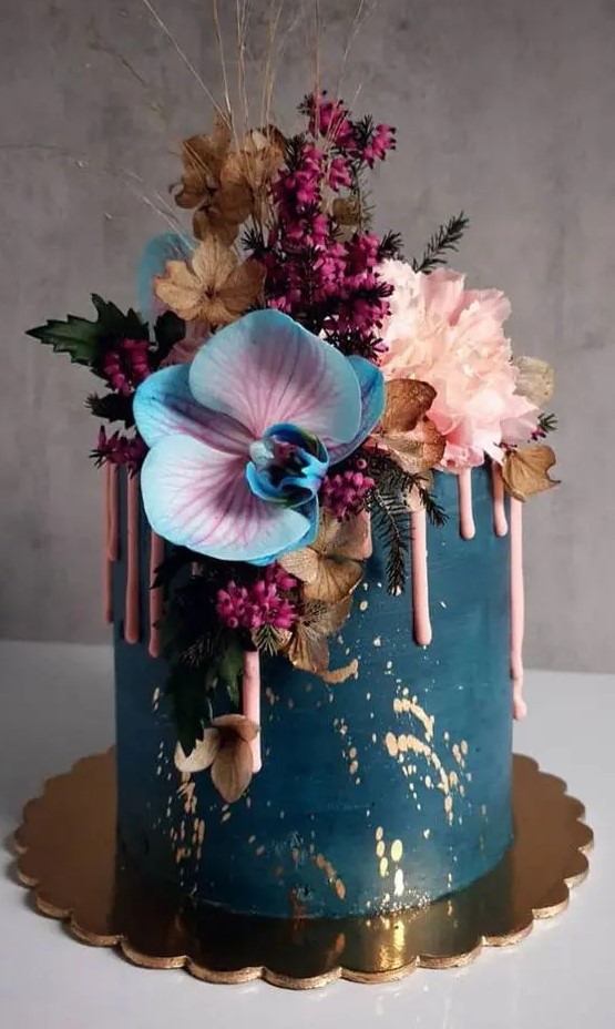 a refined and beautiful navy wedding cake with gold leaf and pink drip, with colorful blooms, berries and dried flowers and twigs
