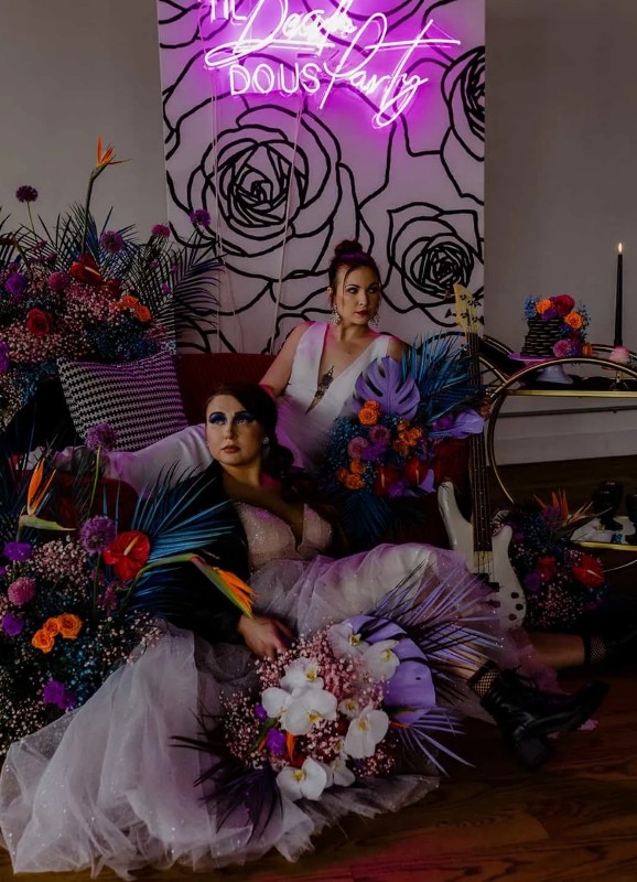 super bold purple wedding decor with a neon sign and bright floral arrangements around, a guitar and some pillows