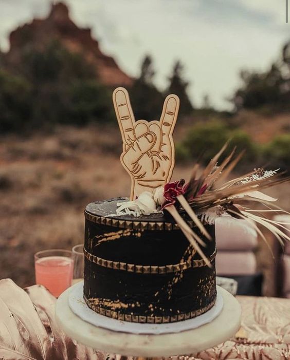a black rock-inspired spiked wedding cake with grasses and blooms and a fun cake topper is a great idea for a rock wedding