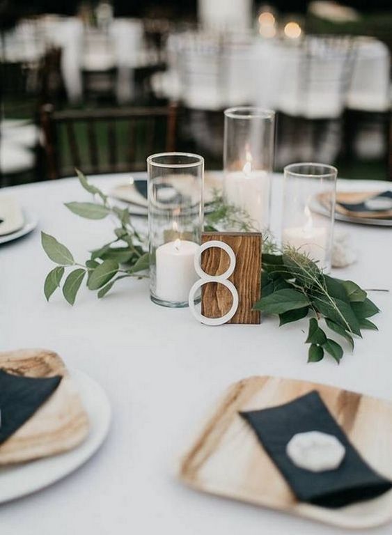a chic minimalist fall wedding tablescape with a table number, pillar candles and greenery, wooden plates and navy napkins
