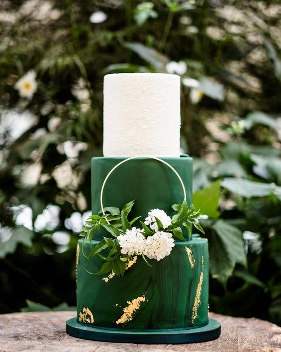 a bright and chic wedding cake in white and emerald, with a marble tier and gold touches, a hoop with greenery and blooms
