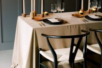 31 a minimalist fall wedding table setting with a beige tablecloth, terracotta candleholders, black plates and gold cutlery