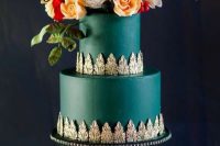 32 a dark green wedding cake with exquisite gold detailing and bold lush blooms and greenery with berries on top