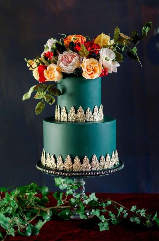 a dark green wedding cake with exquisite gold detailing and bold lush blooms and greenery with berries on top