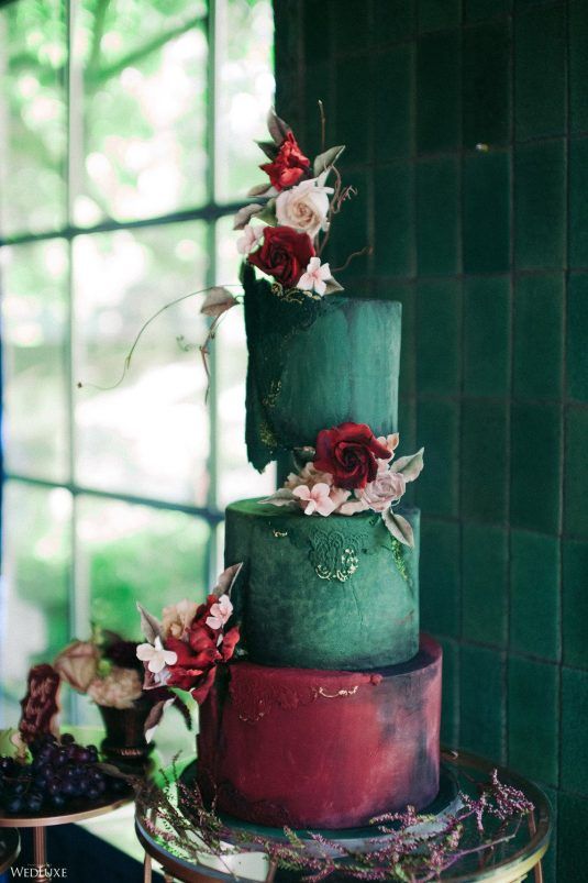a gorgeous and bold wedding cake with green and red tiers, gold detailing, blush and deep red blooms and greenery