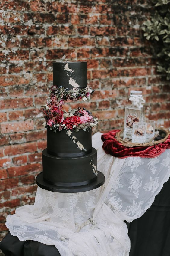 an eye-catchy black rock n roll wedding cake with moody and pink blooms and berries and gold leaf is wow