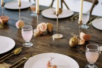 38 a modern to minimal fall wedding tablescape with a naked table, fruit on it and candles, white plates and gold cutlery