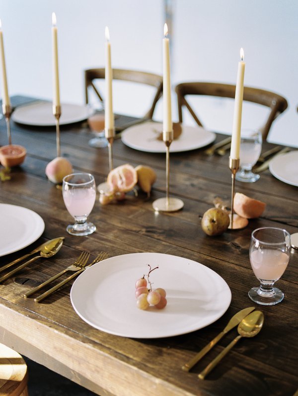 a modern to minimal fall wedding tablescape with a naked table, fruit on it and candles, white plates and gold cutlery