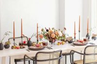 41 a super bold modern wedding tablescape with a bright floral centerpiece, orange candles, black vases and fruit and berries on the table
